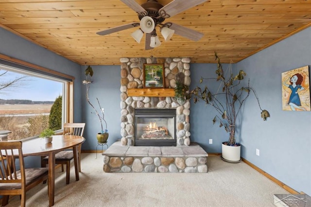 living area featuring a stone fireplace, carpet flooring, a ceiling fan, wood ceiling, and baseboards