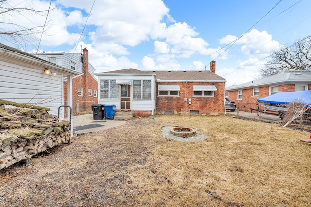 back of house with entry steps, a fire pit, a lawn, fence, and brick siding