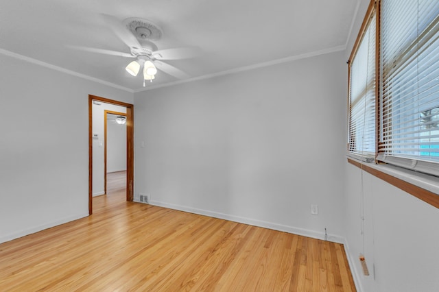 empty room featuring crown molding, visible vents, a ceiling fan, wood finished floors, and baseboards