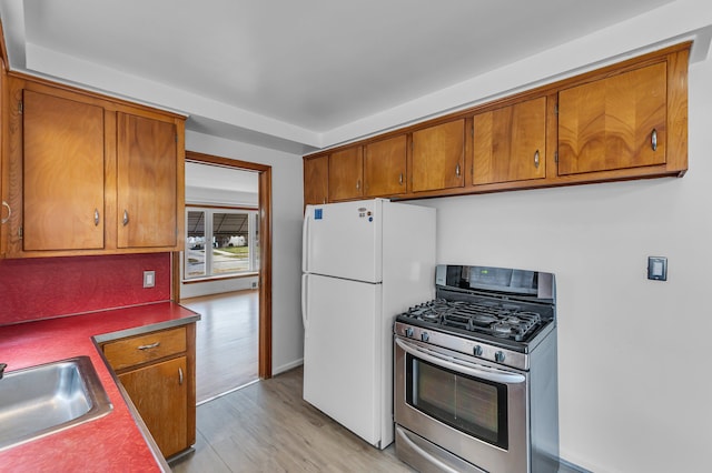 kitchen with freestanding refrigerator, light wood finished floors, brown cabinetry, and gas range