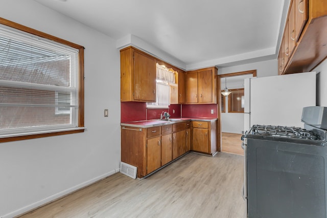 kitchen featuring stainless steel gas range oven, a sink, freestanding refrigerator, and brown cabinets