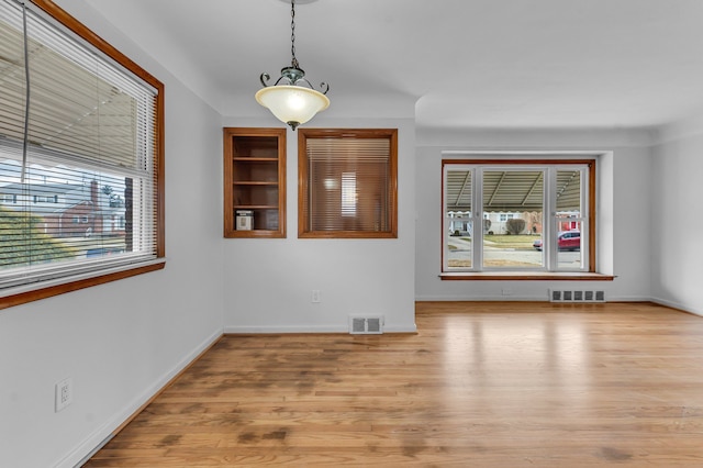 empty room with light wood-type flooring, visible vents, and baseboards