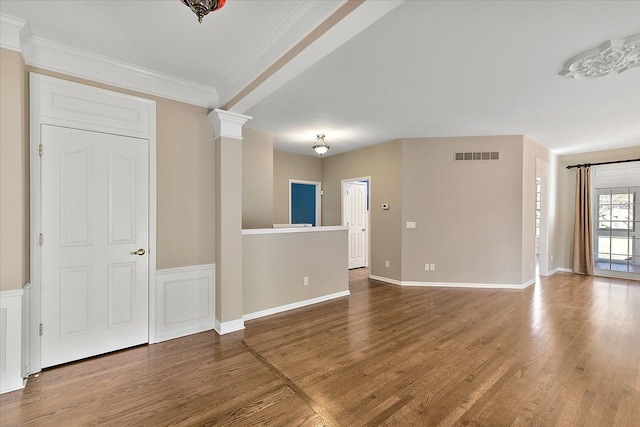 unfurnished living room featuring baseboards, wood finished floors, visible vents, and ornamental molding