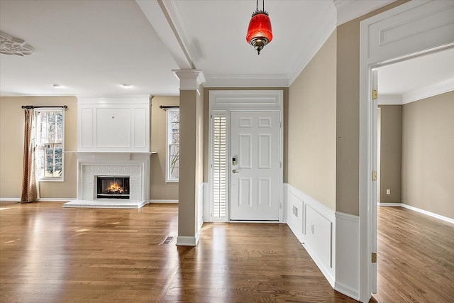 entrance foyer with decorative columns, wood finished floors, and ornamental molding