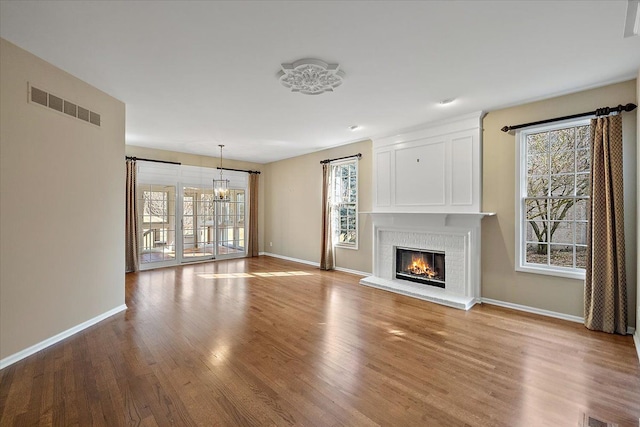 unfurnished living room featuring wood finished floors, visible vents, baseboards, an inviting chandelier, and a fireplace