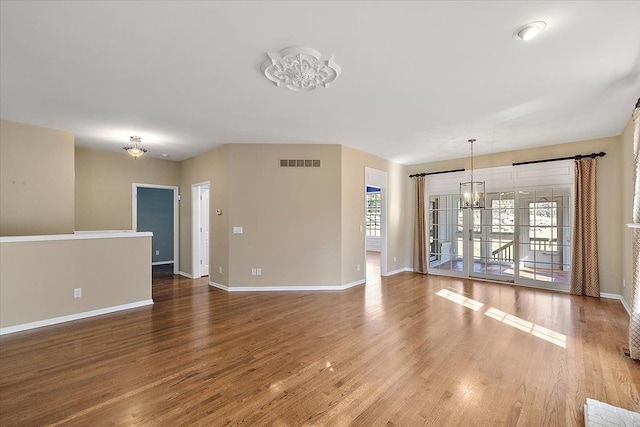 unfurnished living room featuring a notable chandelier, visible vents, baseboards, and wood finished floors