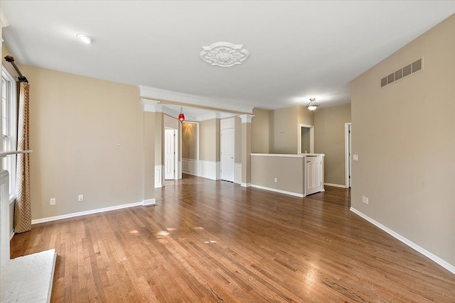 empty room featuring visible vents, baseboards, ornate columns, and wood finished floors