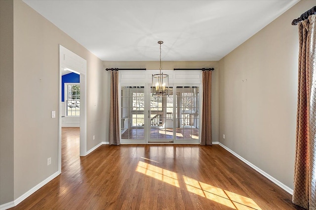 unfurnished dining area featuring baseboards, a notable chandelier, and wood finished floors