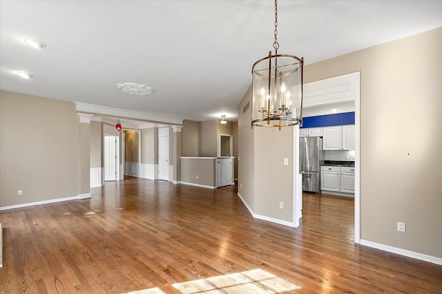 unfurnished living room with a notable chandelier, dark wood-type flooring, baseboards, and decorative columns