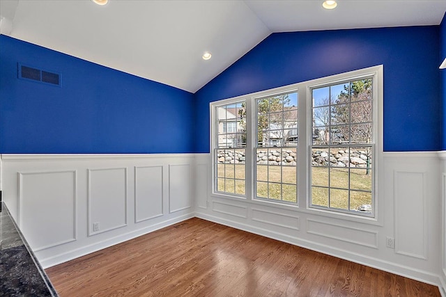 empty room with visible vents, a wainscoted wall, lofted ceiling, and wood finished floors