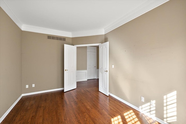 unfurnished room featuring baseboards, wood finished floors, visible vents, and ornamental molding