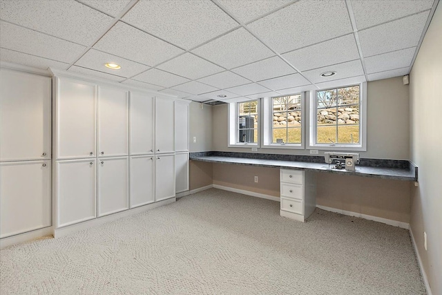 unfurnished office with light colored carpet, built in study area, a paneled ceiling, and baseboards