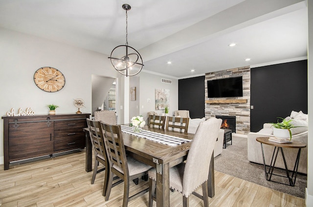 dining area featuring light wood-style floors, visible vents, crown molding, and a stone fireplace