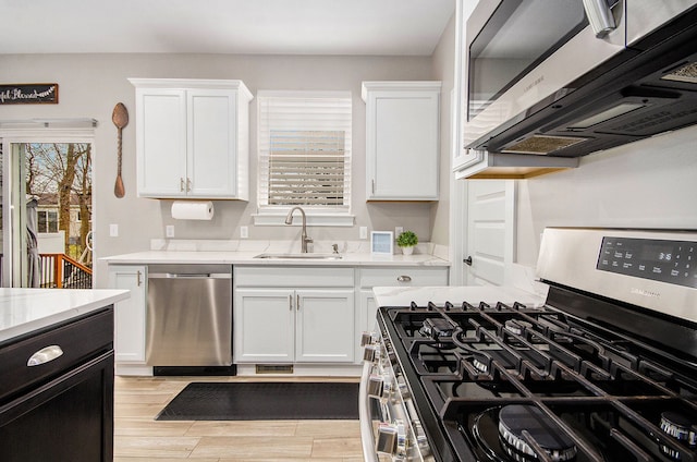 kitchen with stainless steel appliances, white cabinetry, a sink, and light wood-style flooring