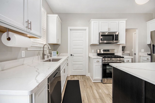 kitchen featuring light wood-style flooring, stainless steel appliances, a sink, white cabinetry, and light stone countertops