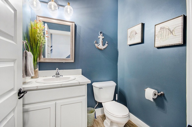 half bathroom with baseboards, vanity, toilet, and wood finished floors