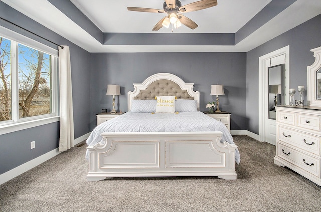 bedroom with ceiling fan, baseboards, a raised ceiling, and dark colored carpet