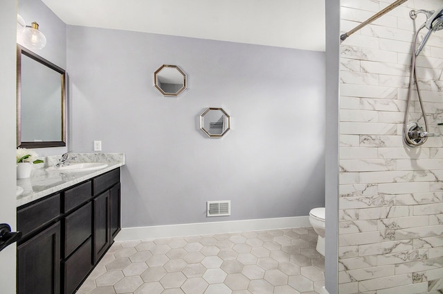 bathroom with baseboards, visible vents, toilet, a tile shower, and vanity