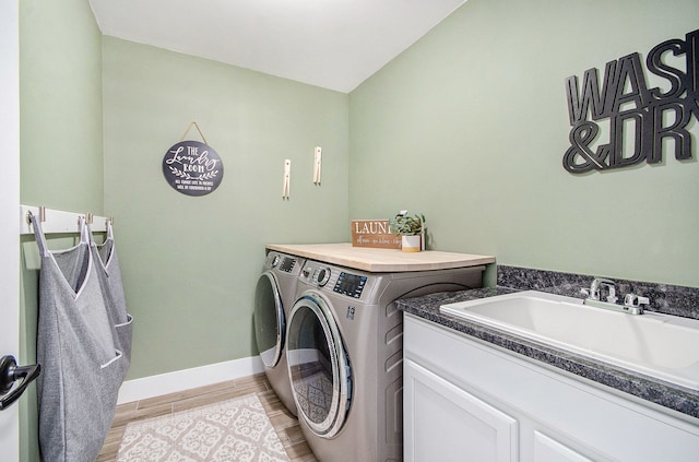 washroom with cabinet space, baseboards, washer and dryer, light wood-style floors, and a sink