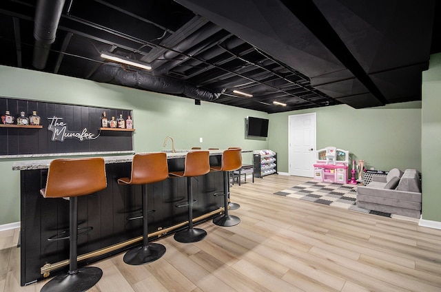 bar with light wood-type flooring, indoor wet bar, a sink, and baseboards