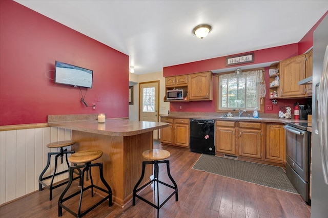 kitchen with a wainscoted wall, dark wood-style floors, appliances with stainless steel finishes, a breakfast bar, and a peninsula