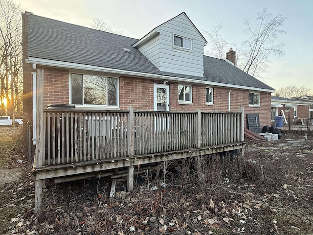 rear view of property featuring a wooden deck, brick siding, roof with shingles, and a chimney