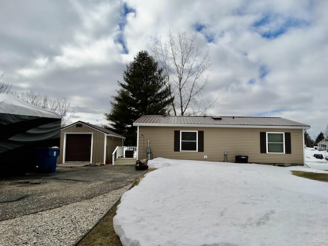 view of front facade with aphalt driveway, metal roof, an outdoor structure, and a detached garage