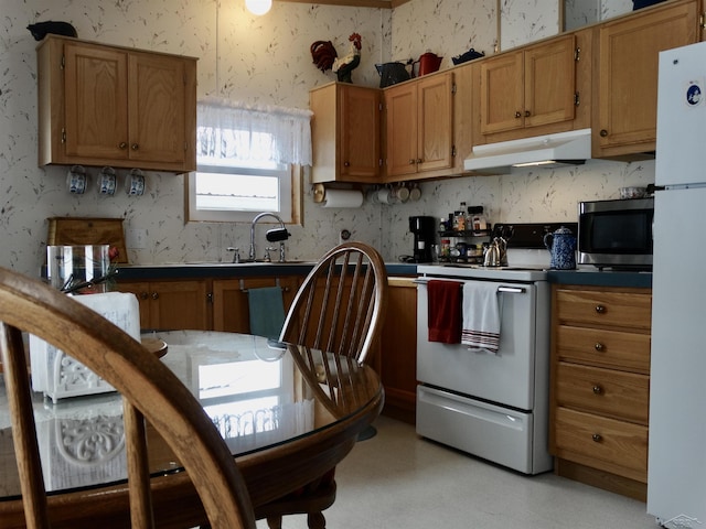 kitchen with under cabinet range hood, white appliances, and wallpapered walls