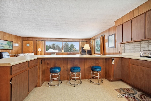 kitchen with open floor plan, light countertops, light floors, brown cabinetry, and a kitchen bar