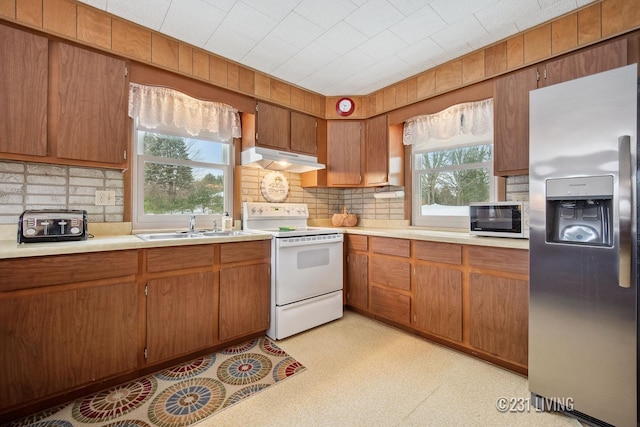 kitchen featuring white appliances, light floors, light countertops, under cabinet range hood, and a sink