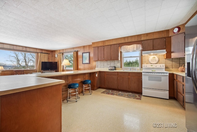 kitchen featuring under cabinet range hood, a wealth of natural light, white range with electric stovetop, and brown cabinets