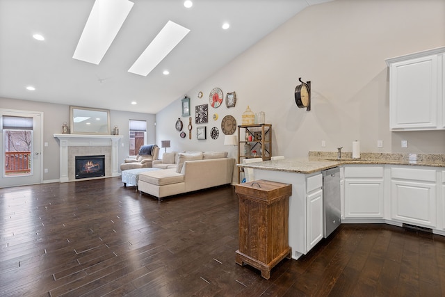 kitchen with light stone counters, vaulted ceiling with skylight, dishwasher, dark wood-style flooring, and a tile fireplace