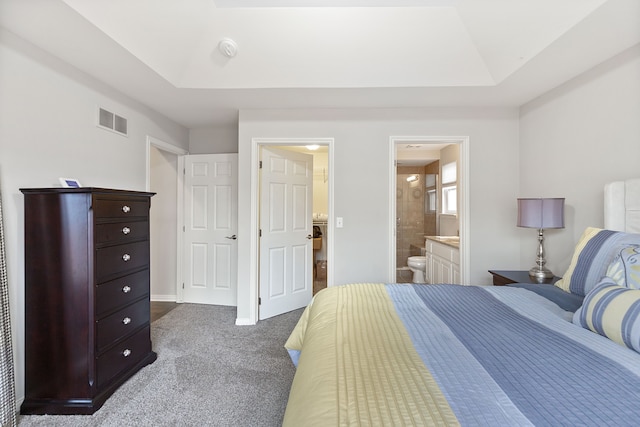 bedroom featuring a raised ceiling, ensuite bathroom, visible vents, and dark carpet