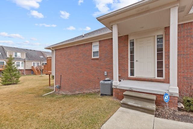 property entrance featuring a yard, brick siding, and central AC unit