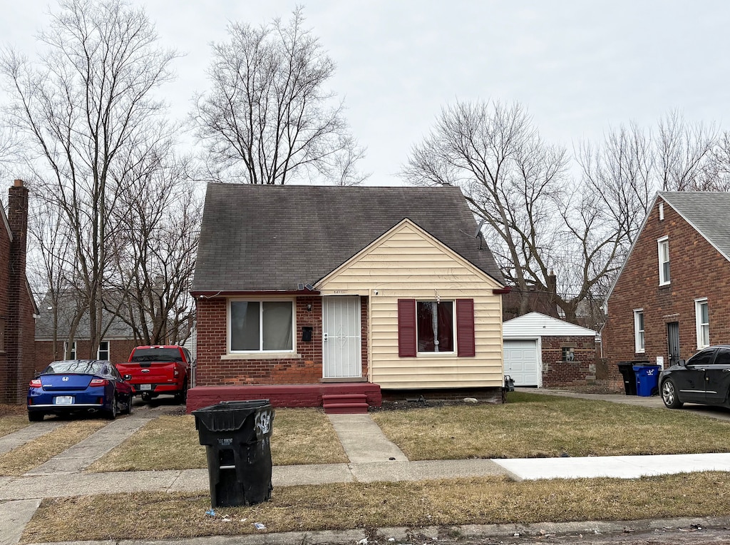 view of front of home with an outbuilding, a detached garage, a front yard, a shingled roof, and brick siding