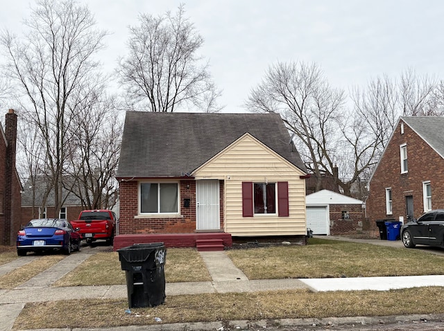 view of front of home with an outbuilding, a detached garage, a front yard, a shingled roof, and brick siding