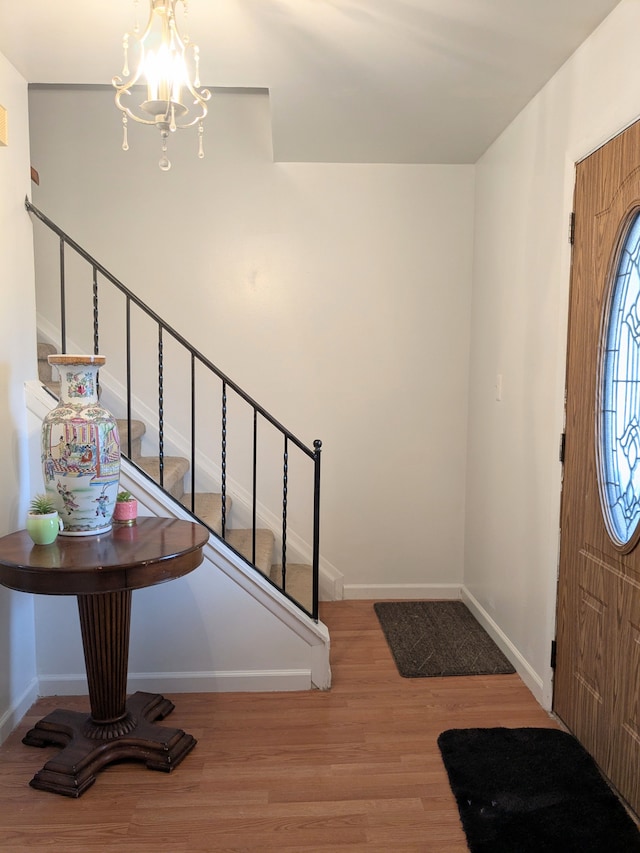 entrance foyer with a chandelier, stairway, wood finished floors, and baseboards