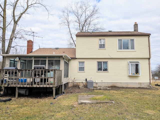 rear view of house with a yard, central AC unit, a chimney, and a sunroom