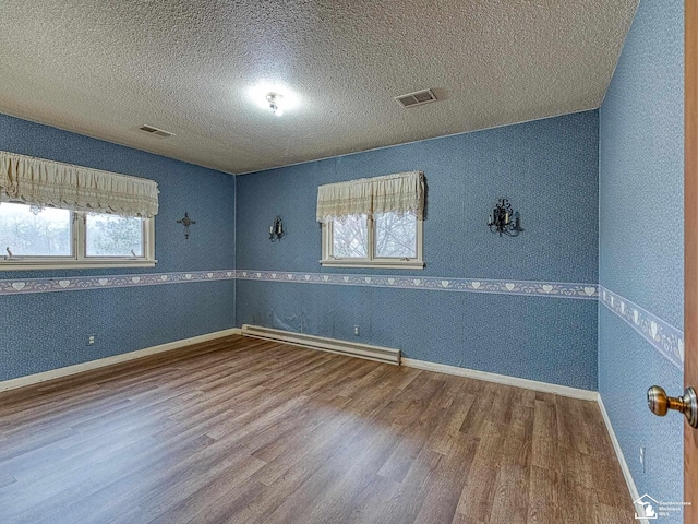 spare room featuring a baseboard heating unit, visible vents, a textured ceiling, and wood finished floors