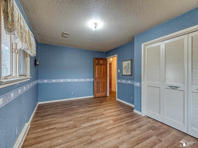 unfurnished bedroom featuring a textured ceiling, wood finished floors, baseboards, a closet, and wallpapered walls