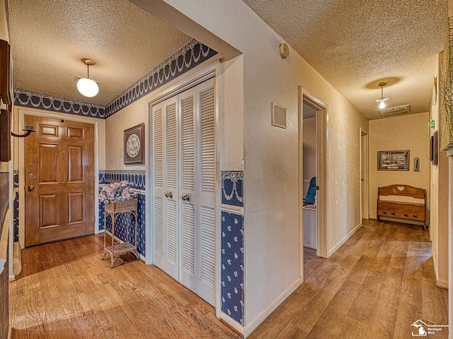 hallway featuring wood-type flooring, a textured wall, a textured ceiling, and baseboards