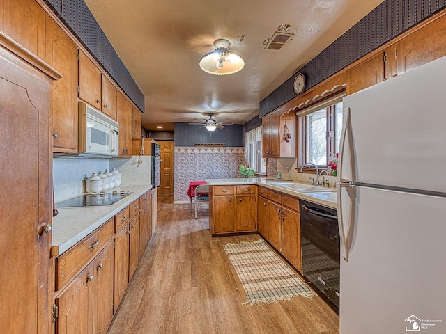 kitchen featuring wallpapered walls, light wood-style floors, light countertops, black appliances, and a sink