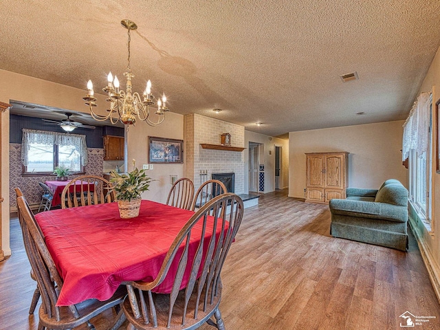 dining area featuring a textured ceiling, light wood finished floors, a fireplace, and visible vents