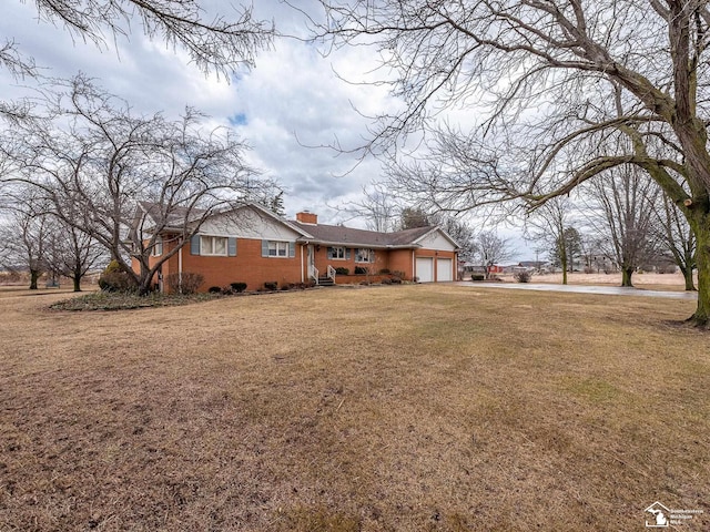 exterior space featuring a garage, driveway, a chimney, a front lawn, and brick siding