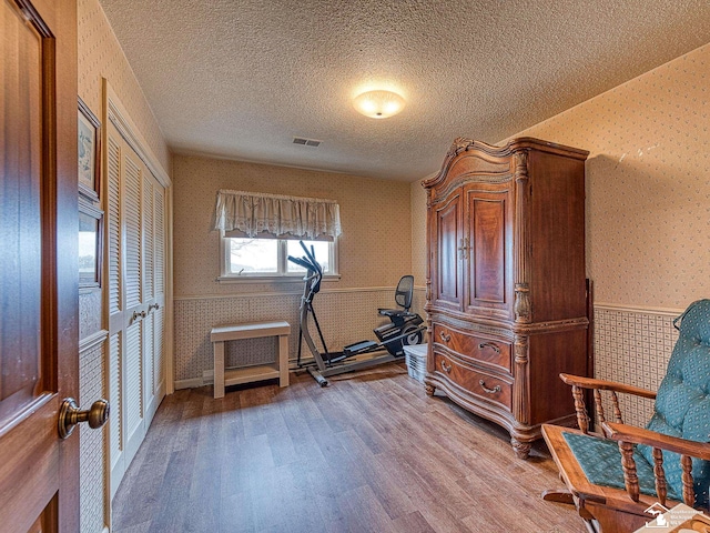 workout area with wallpapered walls, wood finished floors, a textured ceiling, and wainscoting