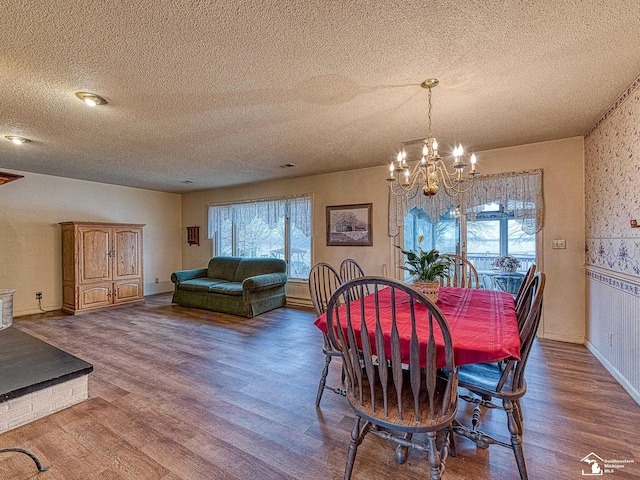 dining space with an inviting chandelier, a textured ceiling, baseboards, and wood finished floors