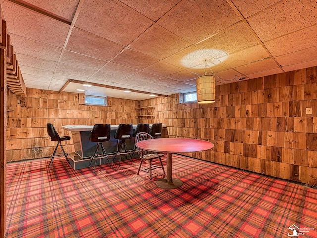 rec room featuring carpet floors, a paneled ceiling, wooden walls, and a dry bar