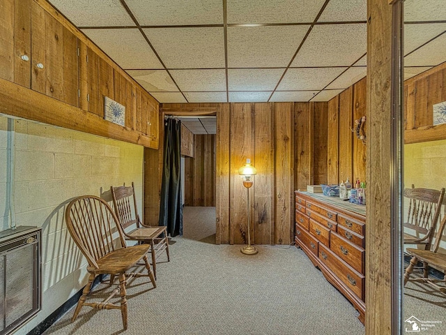 living area with light carpet, heating unit, wooden walls, and a drop ceiling