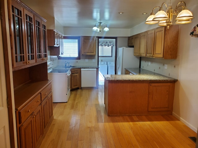 kitchen with white appliances, independent washer and dryer, a peninsula, an inviting chandelier, and a sink