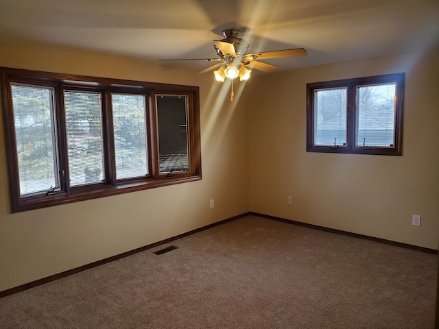 carpeted spare room featuring baseboards, visible vents, and ceiling fan